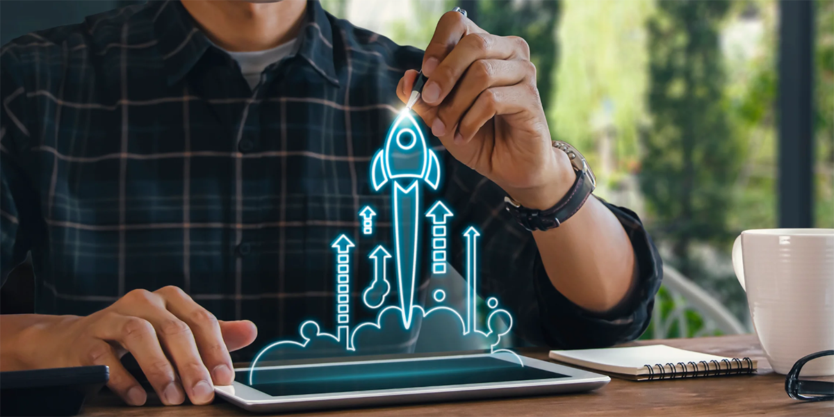 mężczyzna siedzi przy biurku i w powietrzu rysuje wirtualną rakietę