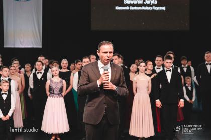Mężczyzna podczas przemówienia, w tle grupa tancerzy